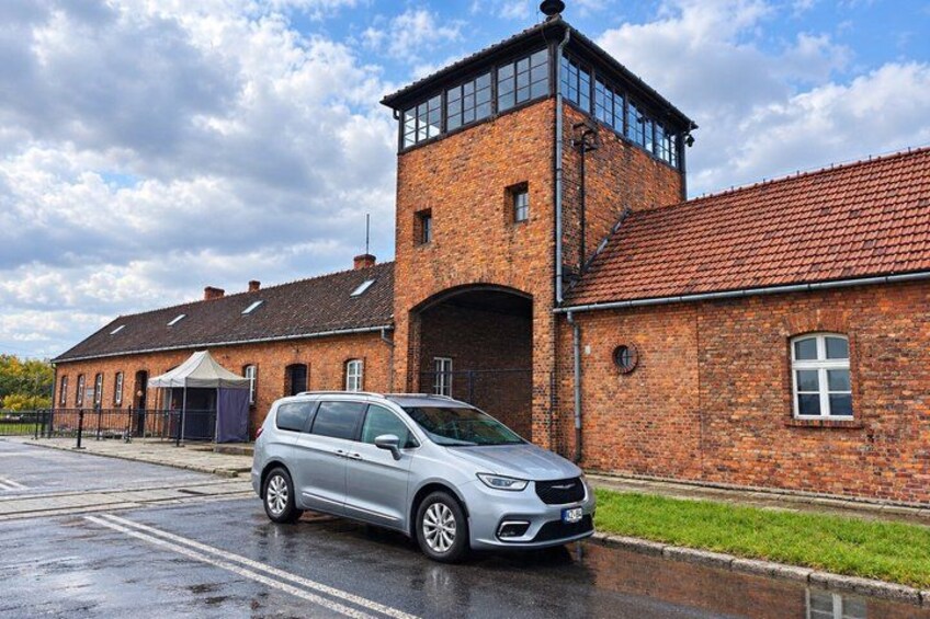 A silver car parked in front of a brick building with a red-tiled roof and a small tower. 4