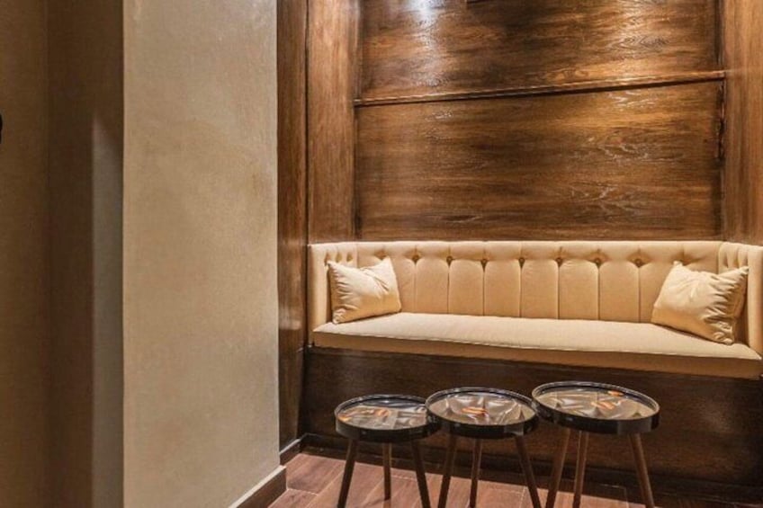 A wooden wall, a beige sofa with cushions, and three small round tables with stools. 4
