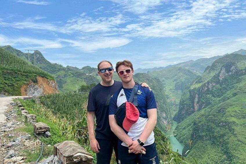 Two people standing on a mountain path with a valley and mountains in the background. 4
