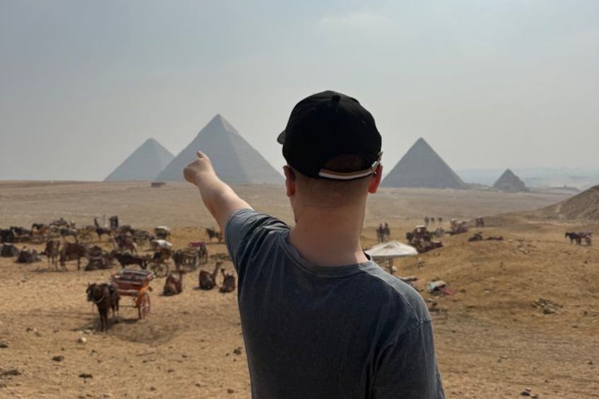A person pointing at the pyramids in the desert with camels in the background. 3