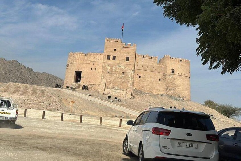Ein weißes Auto vor einer großen, alten Festung mit einer Flagge auf dem Dach. 2