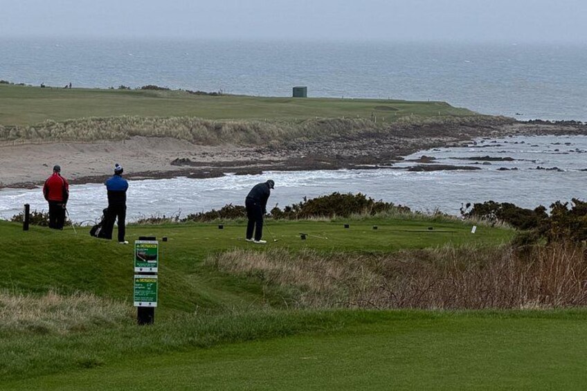 A golf course with players, a signpost, and a view of the sea. 5