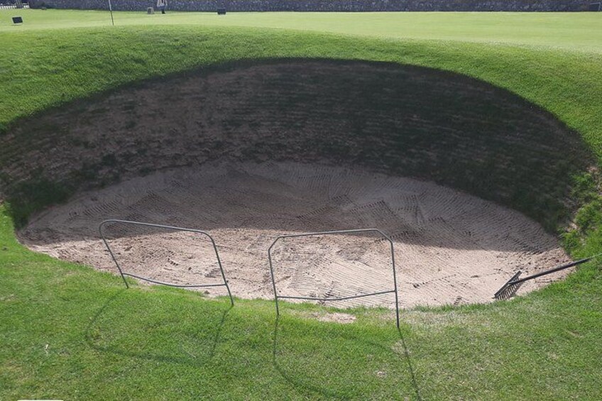 A large, circular depression in a grassy field with a metal fence around it. 4