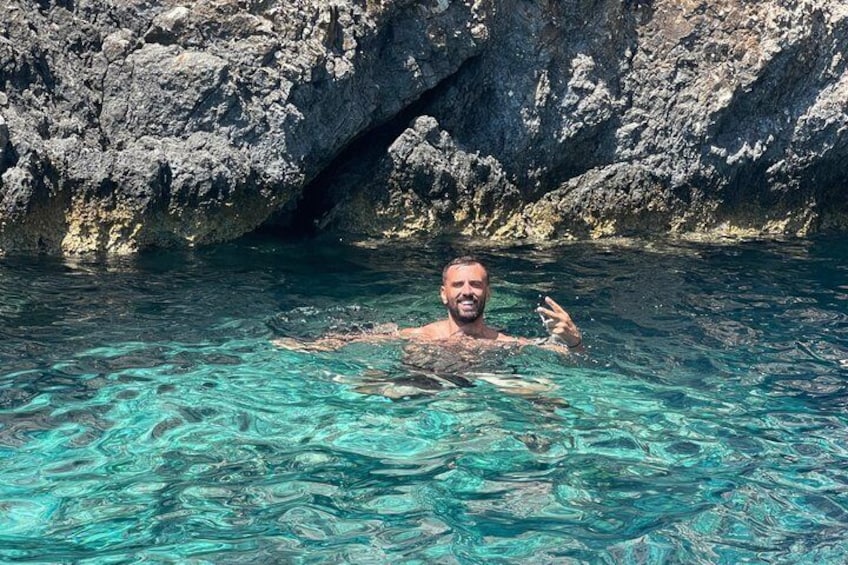 A person swimming in clear blue water with rocky cliffs in the background. 2