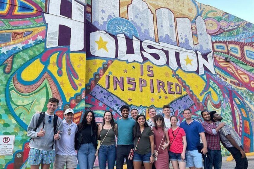 A group of people posing in front of a colorful mural with the text "Houston is Inspired". 1