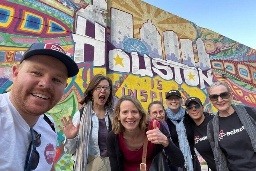 A group of people in front of a colorful mural with the word "Houston" and the phrase "Houston Inspires." 2