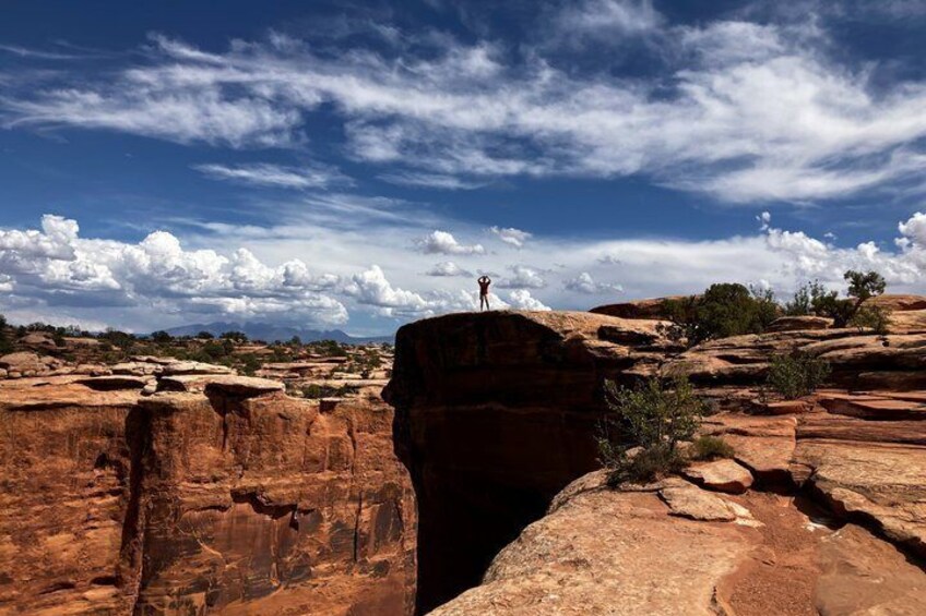 A person standing on a rock formation with a vast landscape and clouds in the sky. 4