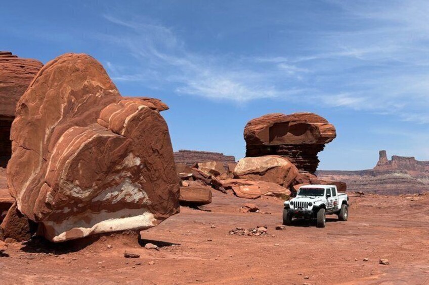 A white off-road vehicle in a desert landscape with large red rock formations. 1