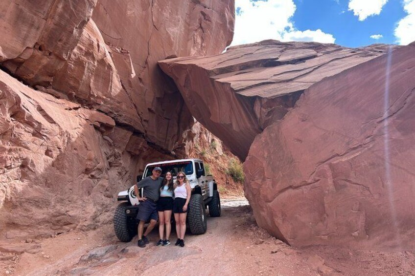 A vehicle navigating a narrow canyon with large red rock formations. 5