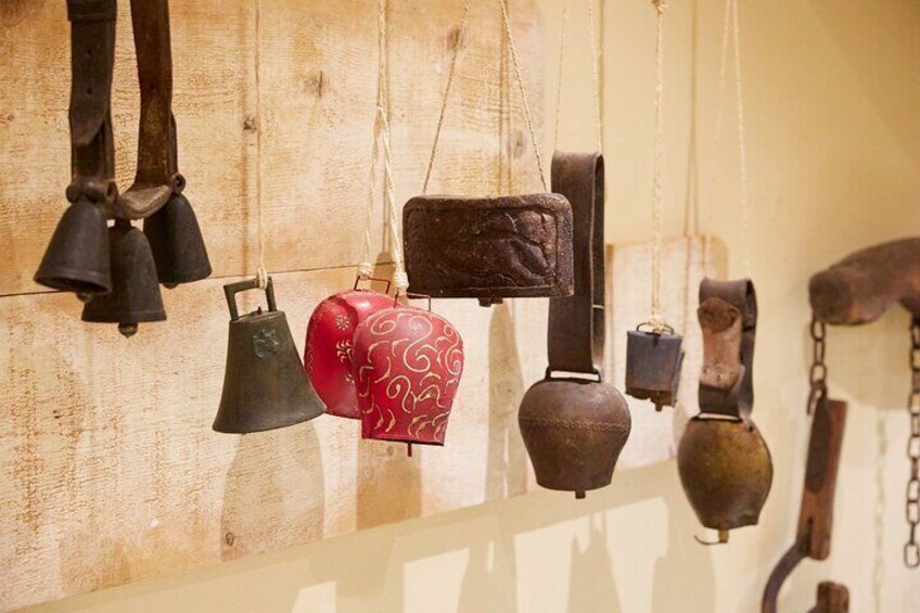 Een verzameling antieke klokken en bellen hangt aan een houten muur. 5