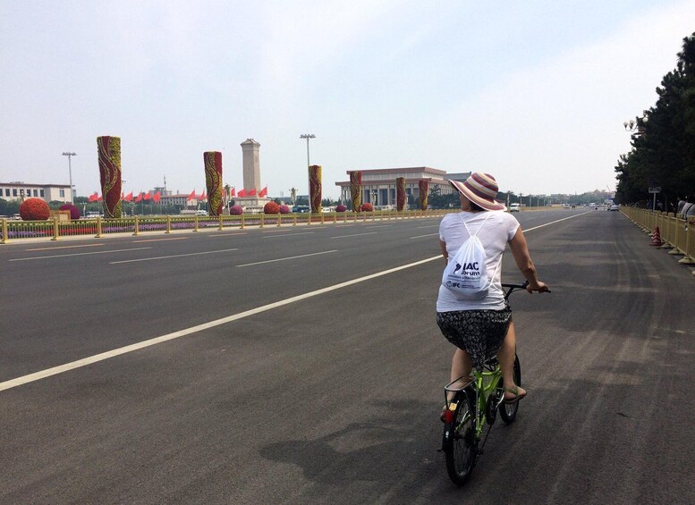 A person riding a bicycle on a wide road with a fence on one side and a building with a flag on the other. 5
