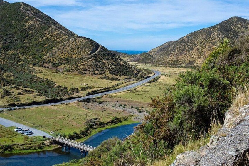 Une route sinueuse traverse une vallée, enjambant une rivière grâce à un pont, et est bordée de collines et de verdure. 2