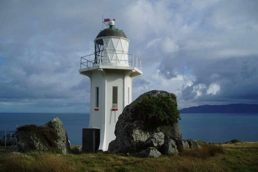 Un phare blanc, surmonté d’un drapeau rouge, entouré de rochers et d’herbe. 3