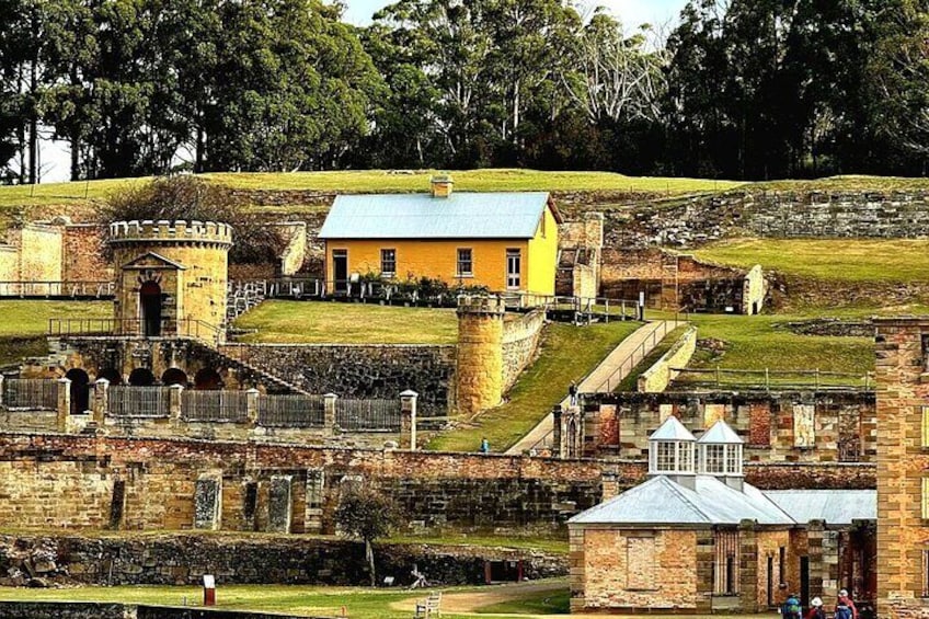 A historical site with a yellow building, stone walls, and a tower. 1