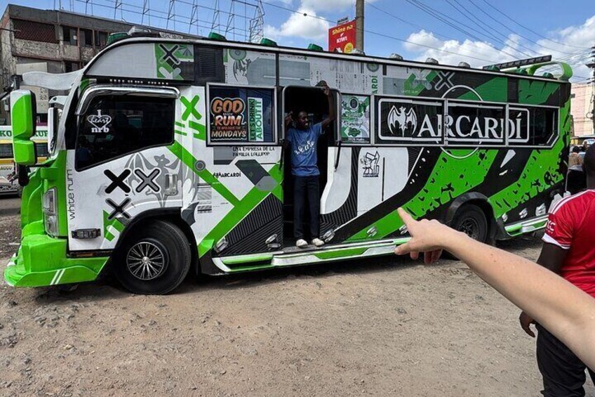 Een groene en witte bus met 'GOD RUM MONDAYS' en 'ARCARDI' logo's, geparkeerd op een onverharde weg. 1