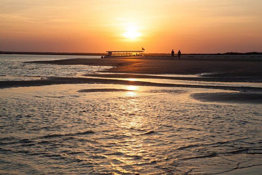 Tramonto su una spiaggia con onde, un molo e due persone che passeggiano. 2