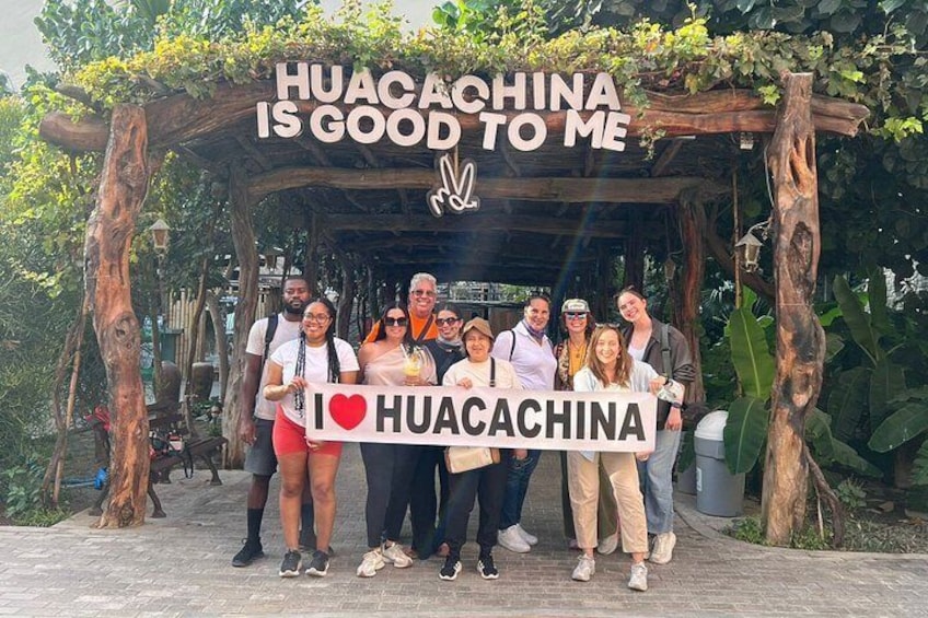 En gruppe mennesker står under en trækonstruktion med et banner, der siger 'I ♥ HUACACHINA IS GOOD TO ME'. 1