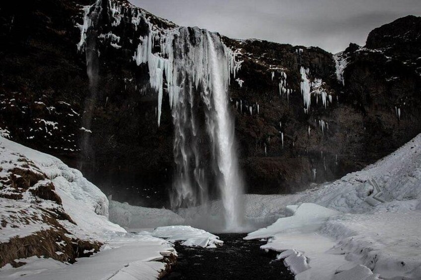 A waterfall cascading into a snow-covered valley with icicles hanging from the cliff. 1