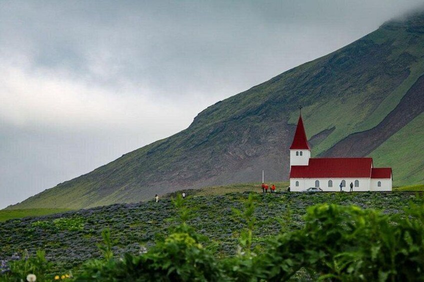 A church with a red roof and white walls, surrounded by a green landscape with a mountain in the background. 2