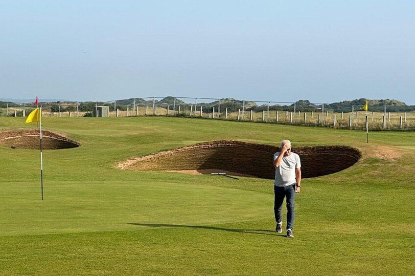 Ein Golfplatz mit einer Fahne, einer Person, die geht, und Sandbunkern. 5