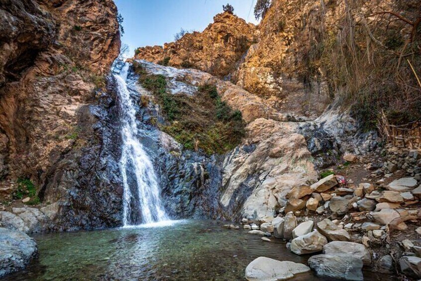 A waterfall cascading down a rocky cliff into a pool surrounded by boulders and sparse vegetation. 3