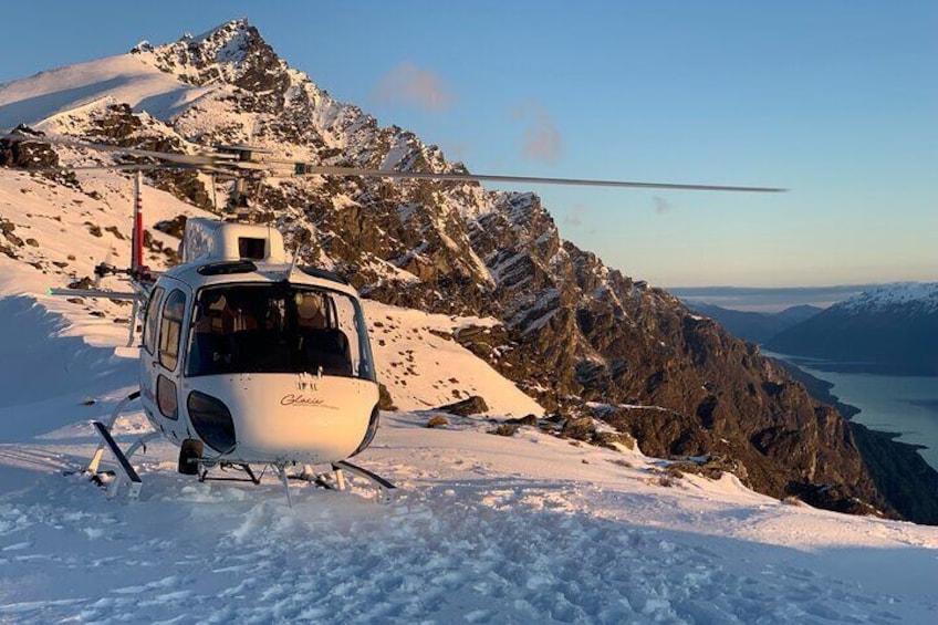 A helicopter on a snowy mountain with a clear sky and a lake in the background. 1
