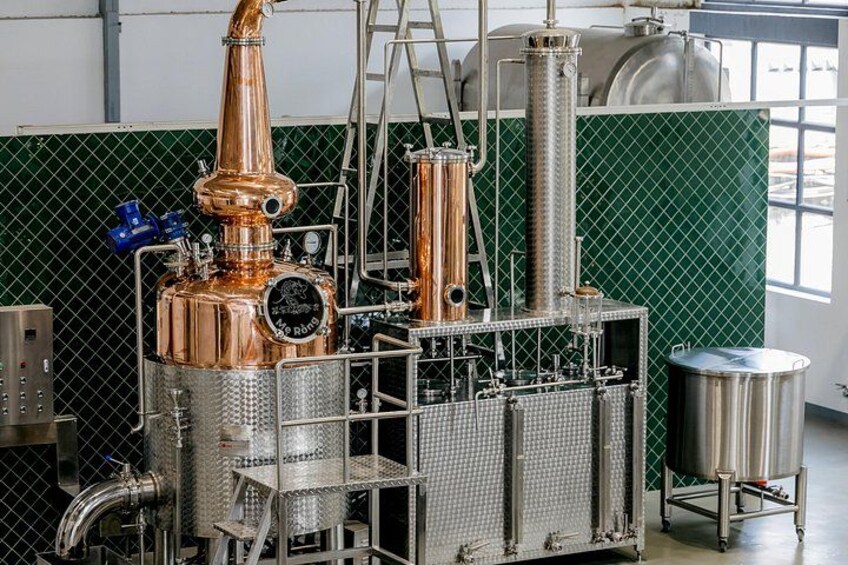 A copper distillation apparatus with a large copper still, a silver cylindrical vessel, and a metal mesh structure. 5