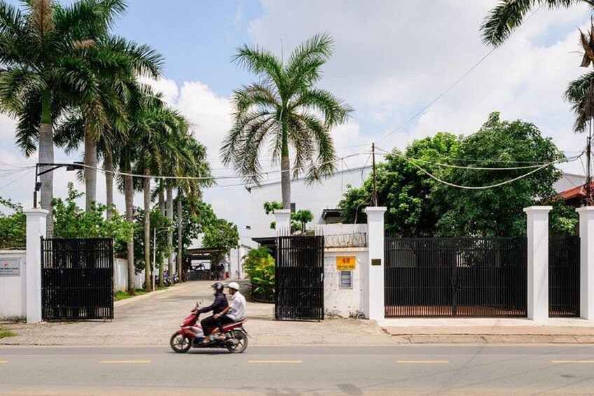 A street with a motorbike, palm trees, and a gated entrance. 2