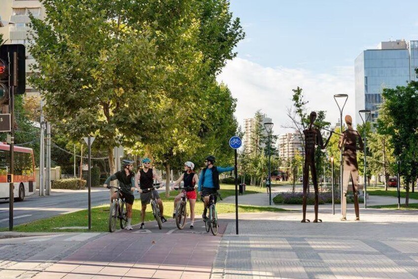 Un groupe de cyclistes sur un trottoir de la ville, avec des arbres et des bâtiments en arrière-plan. 1