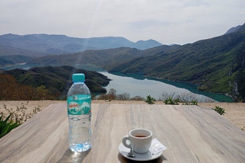 En vattenflaska och en kopp kaffe står på ett bord med en vacker utsikt över en sjö och berg i bakgrunden. 2