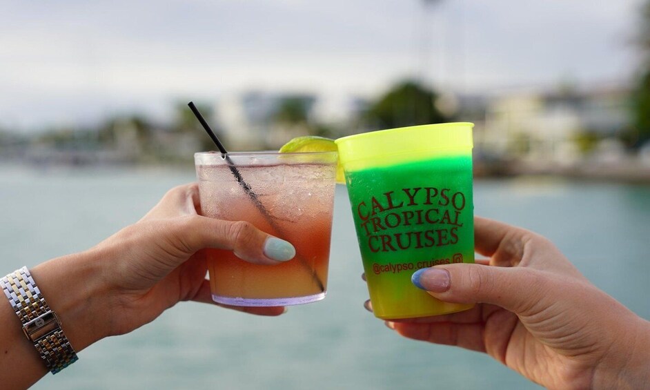Two hands holding a glass of drink and a cup with 'CALYPSO TROPICAL CRUISES' text. 5
