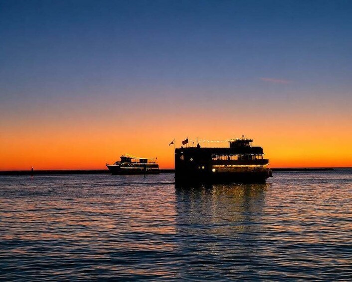 A sunset over calm waters with two boats silhouetted against the sky. 2