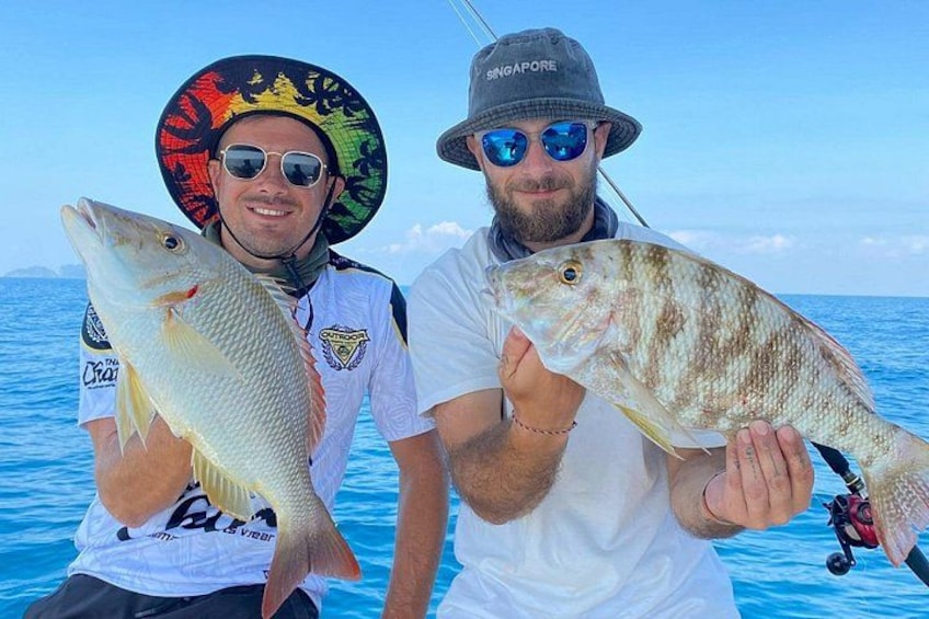 Deux personnes tenant des poissons sur un bateau, avec un ciel bleu clair et l’océan en arrière-plan. 4