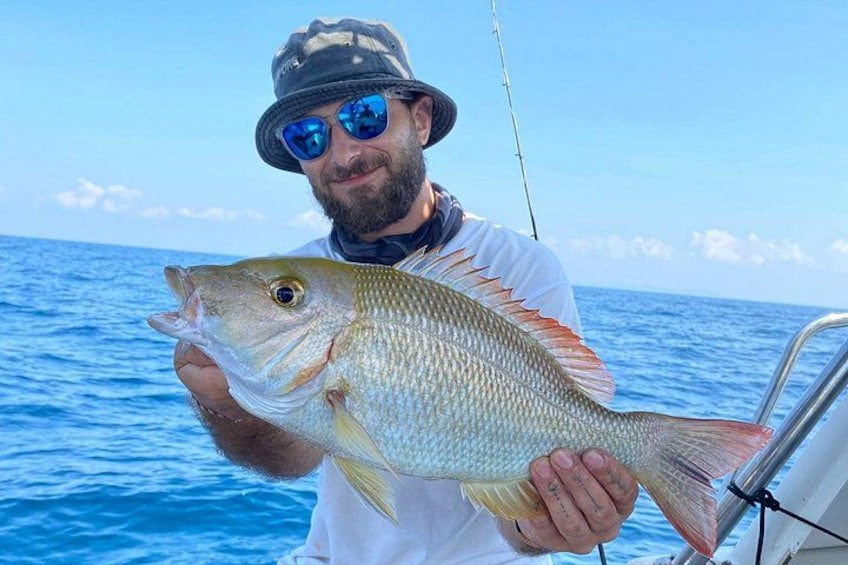 Une personne tenant un poisson sur un bateau, avec l’océan en arrière-plan. 5