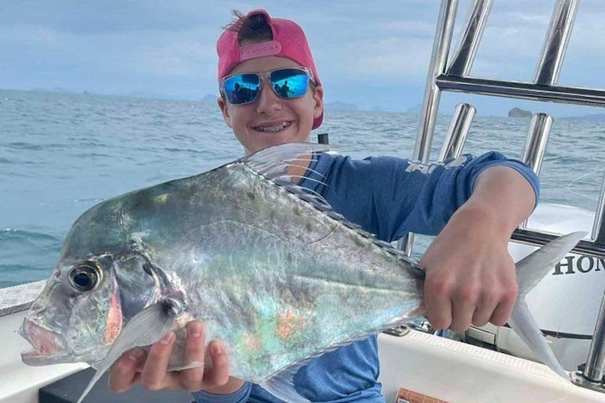 Une personne tenant un gros poisson sur un bateau, avec l’océan en arrière-plan. 2