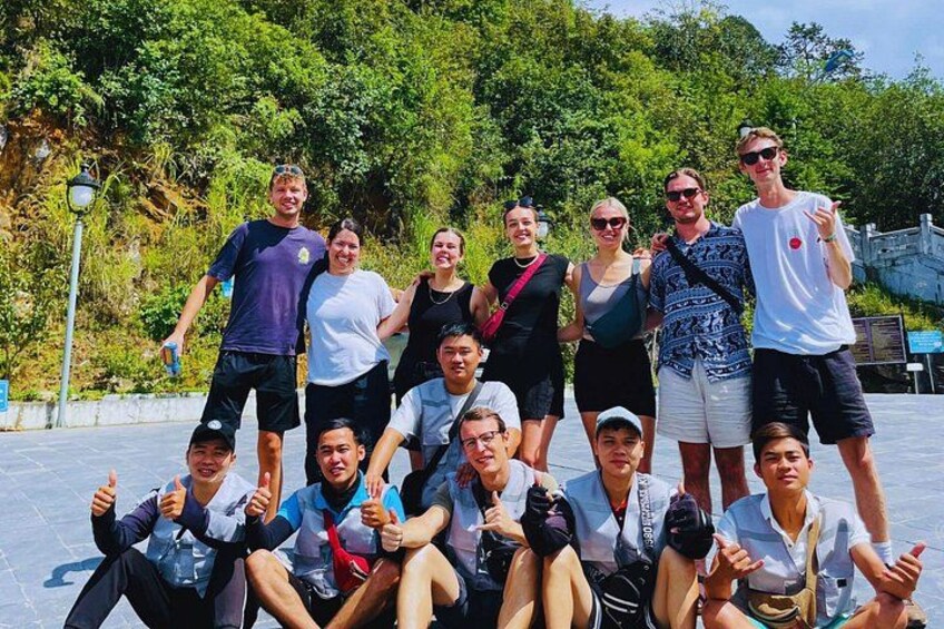 Eine Gruppe von Personen posiert für ein Foto in einer natürlichen Umgebung mit Bäumen und einer gepflasterten Fläche. 2