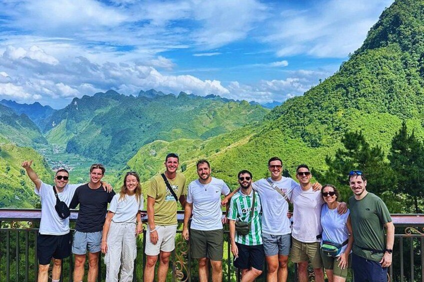 Eine Gruppe von Menschen steht auf einer Brücke, im Hintergrund eine Berglandschaft. 3