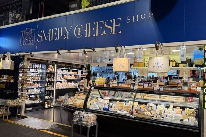 Una bottega di formaggi con un cartello blu, scaffali pieni di formaggio e sacchetti appesi. 2
