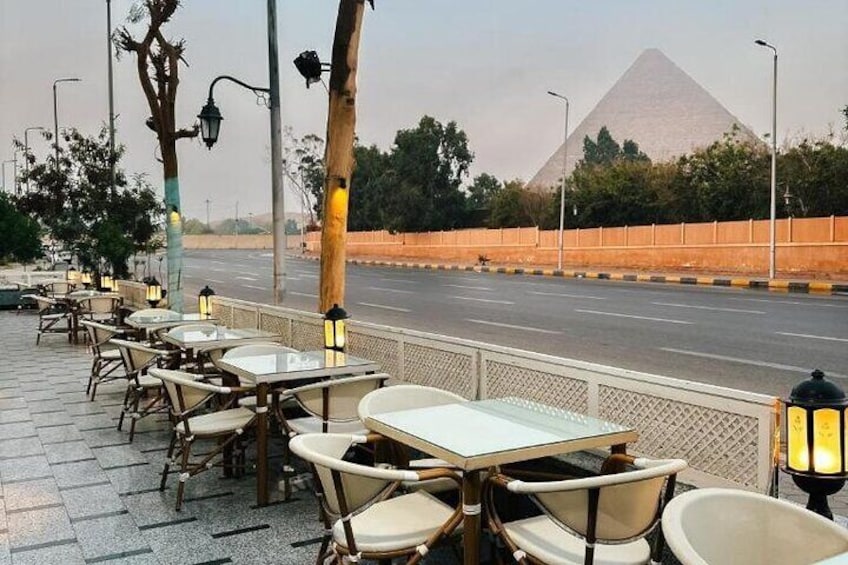 Tavolini e sedie di un caffè all'aperto, una strada e una piramide sullo sfondo. 3