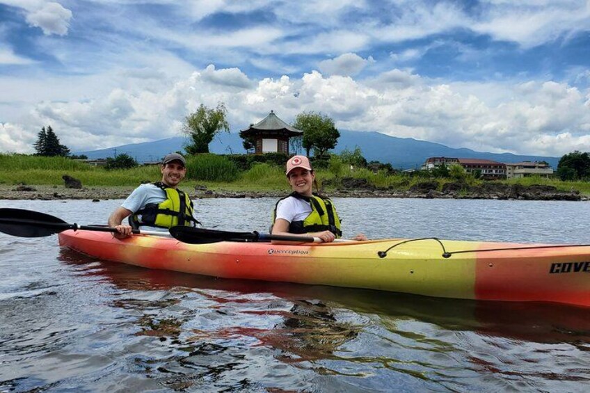 Two people in a kayak on a calm body of water with a house and mountains in the background. 5