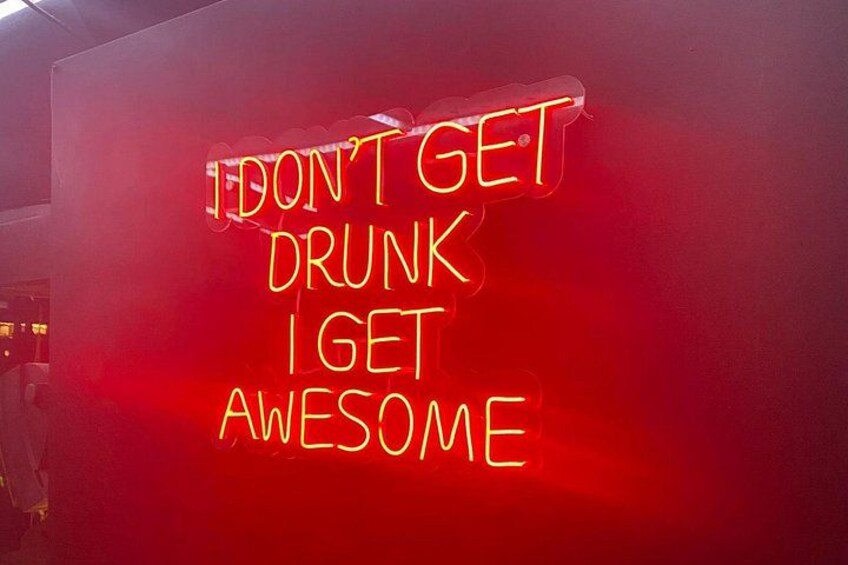 A red wall with a neon sign that reads 'I don't get drunk, I get awesome.' 2