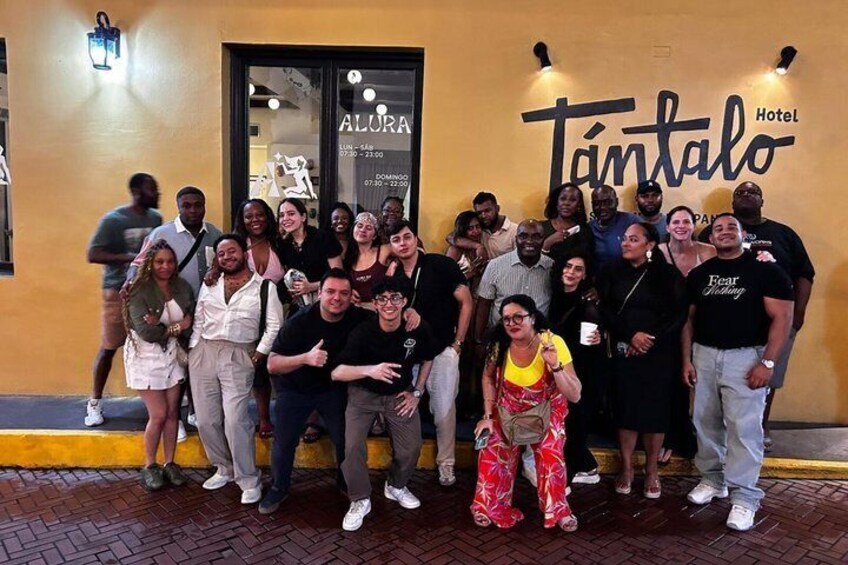 A group of people posing in front of a building with a sign that reads 'Tántalo Hotel.' 1