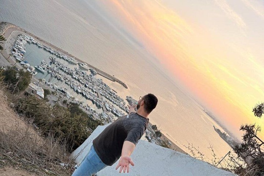 Eine Person blickt auf einen Yachthafen mit Booten und einem Sonnenuntergang. 2