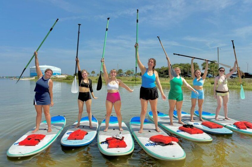 A group of people paddleboarding on calm water with paddleboards and life vests. 3