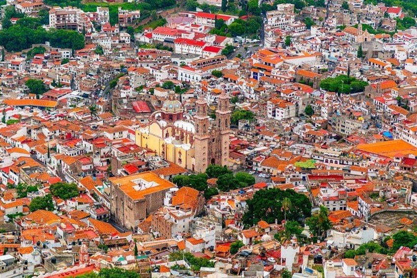 Un'area urbana densamente popolata con numerosi edifici, una chiesa importante con un campanile e un mix di tetti rossi e bianchi. 2