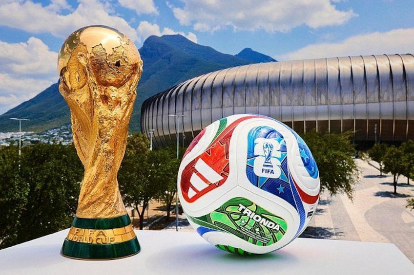 Un trofeo dorato e un pallone da calcio con marchio FIFA, con uno stadio moderno e montagne sullo sfondo. 5