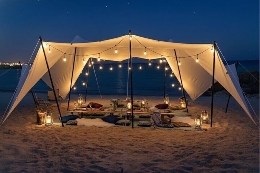 A tent set up on a beach at night with string lights and lanterns. 4