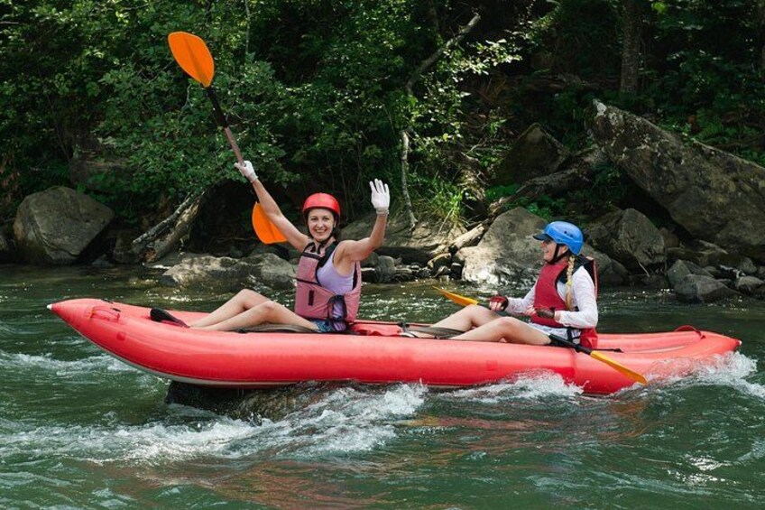 Zwei Personen paddeln mit einem Kajak auf einem Fluss, umgeben von Felsen und viel Grün. 5