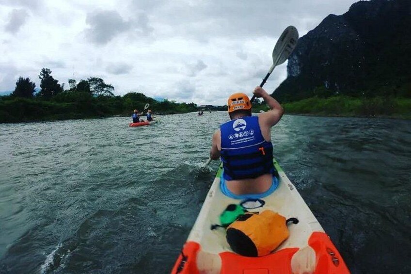 Eine Person paddelt mit einem Kajak auf einem Fluss, im Hintergrund ist ein weiteres Kajak zu sehen. 2