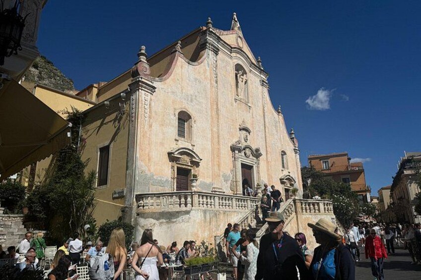 A historic building with a staircase leading to the entrance, surrounded by people. 4